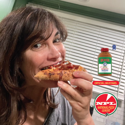 A woman eating pizza with a bottle of peanut butter in front.