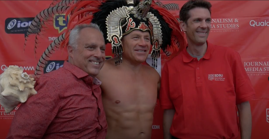 Three men standing next to each other in front of a red wall.