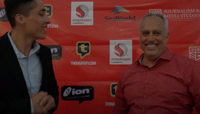 Two men standing in front of a red wall.